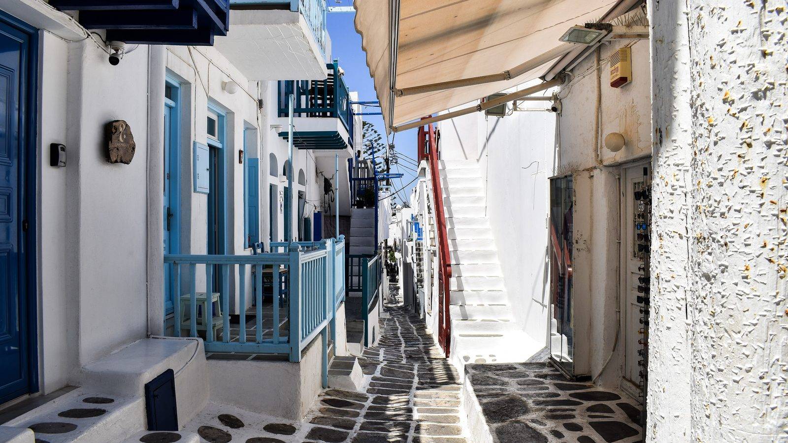 A narrow lane of Mykonos Town with blue balconies, white stairs and a paved path