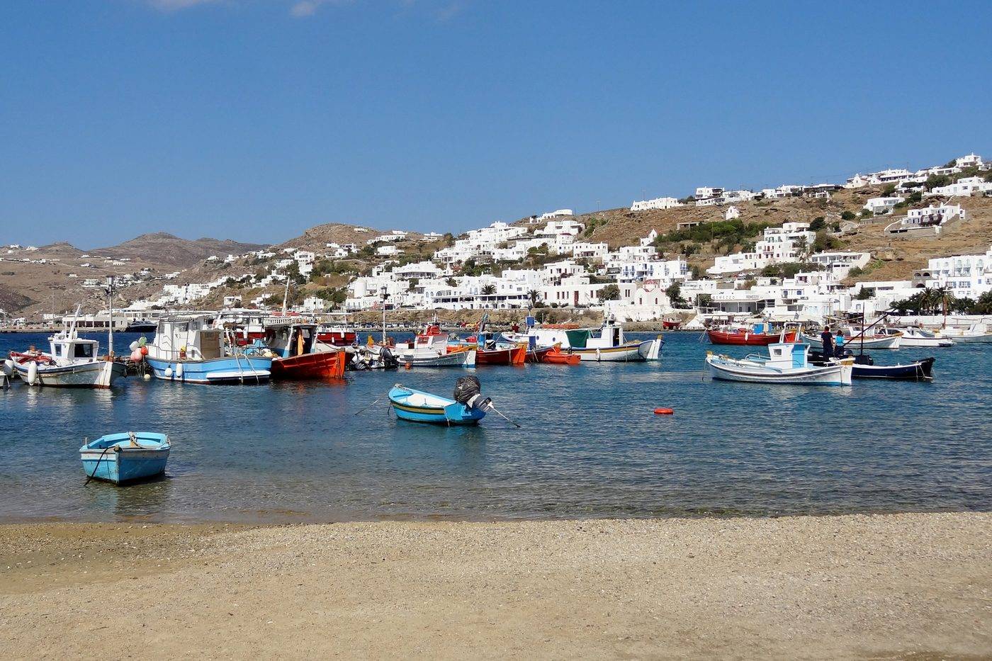 Fishing boats moored in the old harbour of Mykonos Town, with the white houses on the hill above