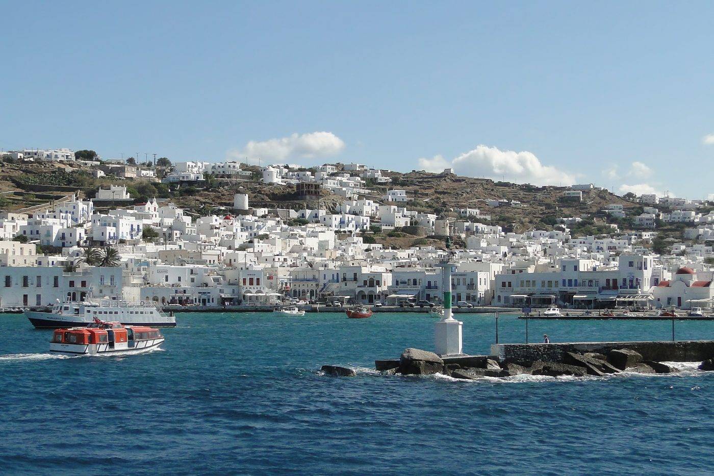 Boats crossing the Old Port of Mykonos, with the white houses of Mykonos Town on the hill behind