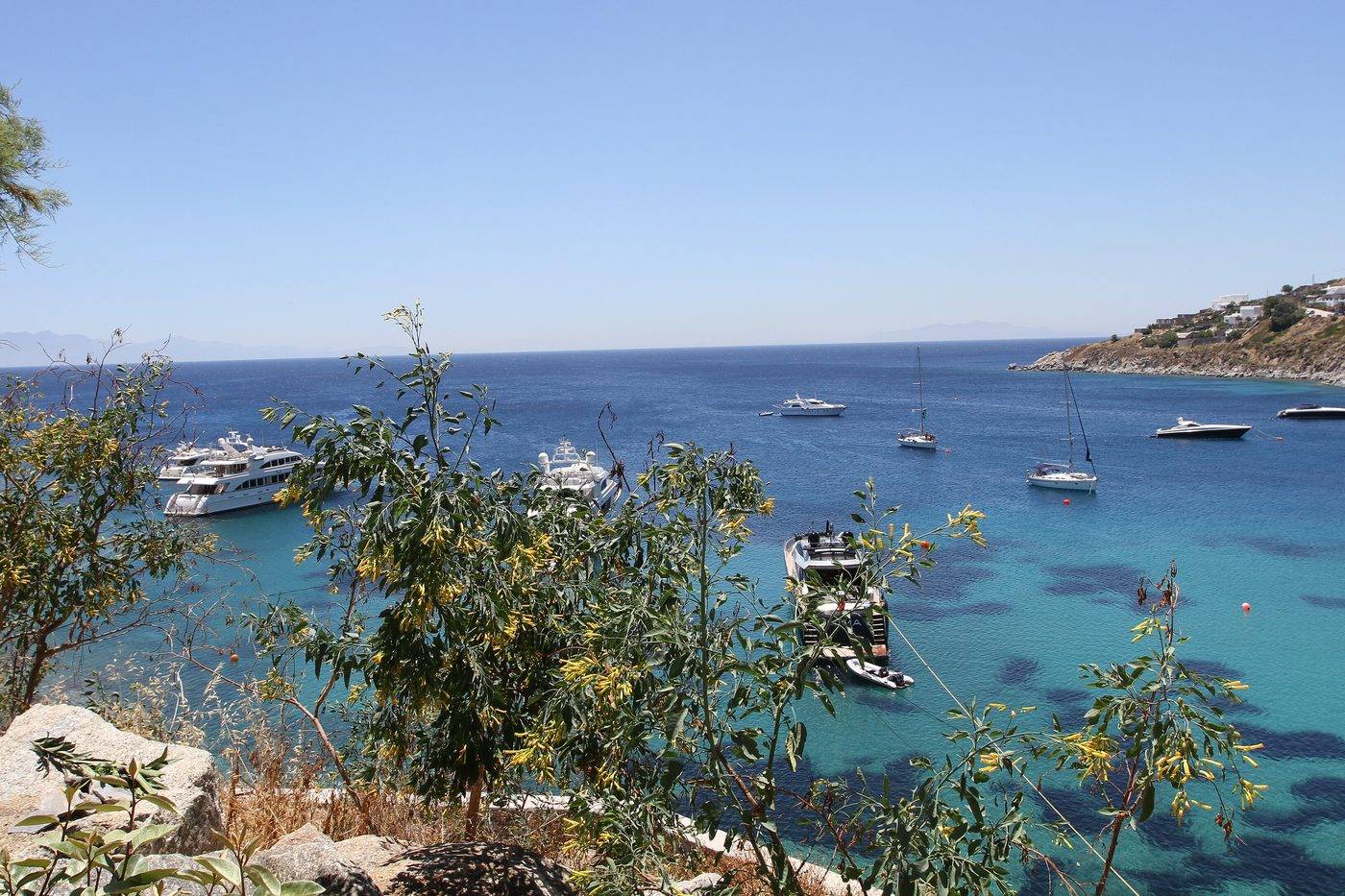 Yachts and sailing boats anchored in the turquoise bay of Platis Gialos, seen through the trees