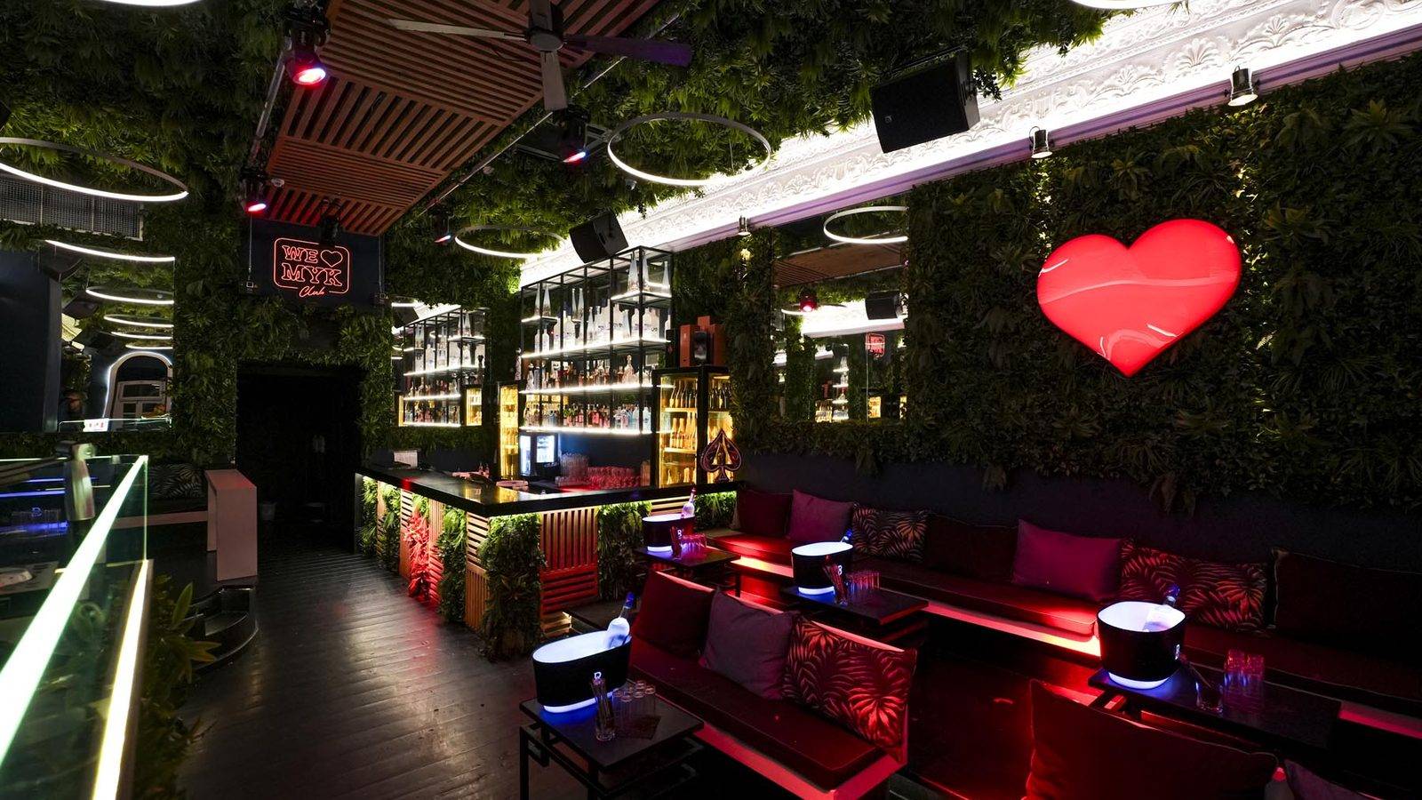 Inside WE ❤ MYK Club: red sofas, a plant wall and the glowing red heart, with the bar behind