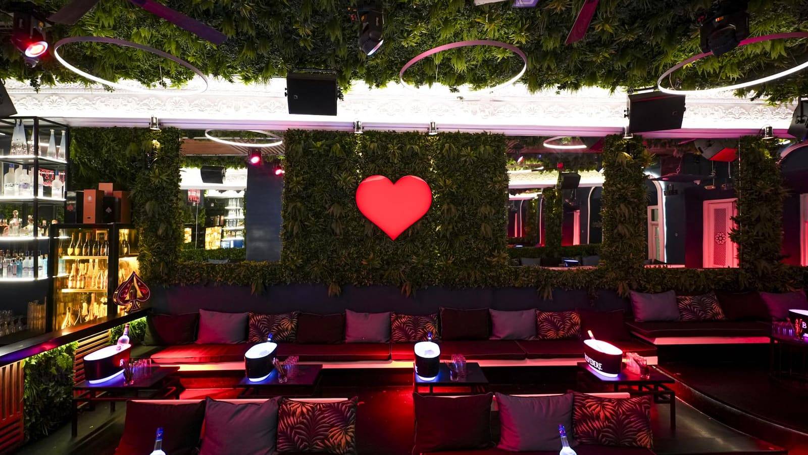 The lounge of WE ❤ MYK Club in Mykonos Town, with the red heart on the plant wall and the sofas lit in red
