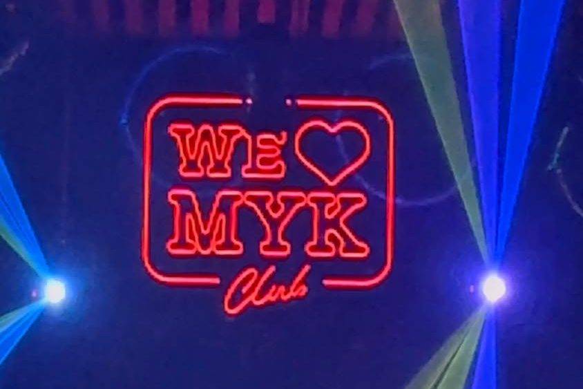The red neon WE ❤ MYK Club sign with blue laser beams on the dancefloor