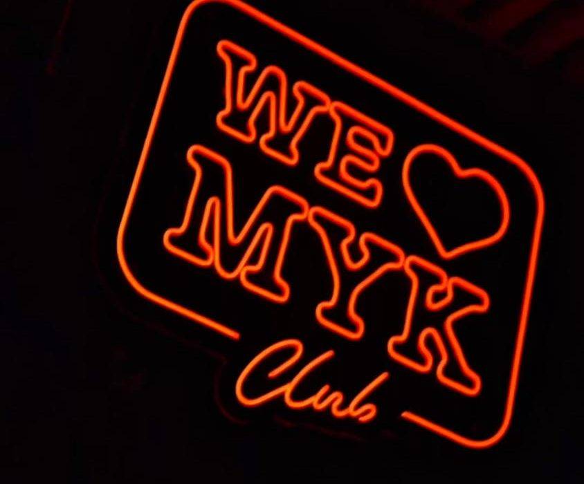 The red neon WE ❤ MYK Club sign glowing in the dark