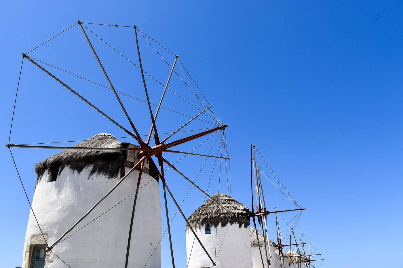 Two Mykonos windmills with thatched roofs and wooden sails against a blue sky