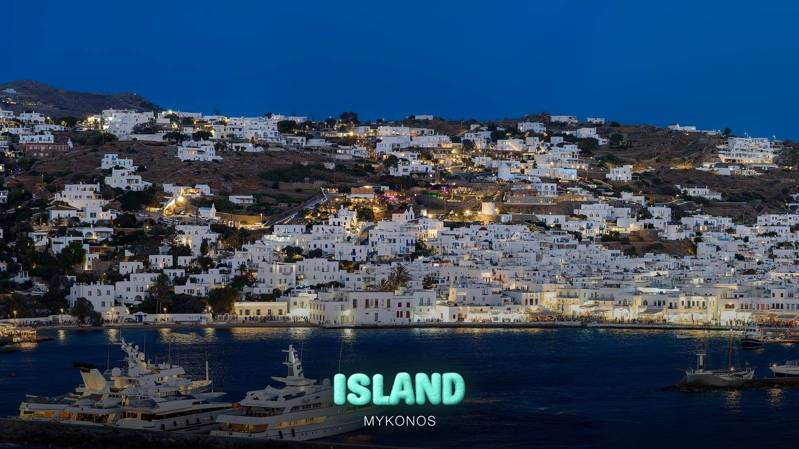Yachts moored in Mykonos harbour at dusk, with the lights of Mykonos Town behind, with the Party Island Mykonos logo