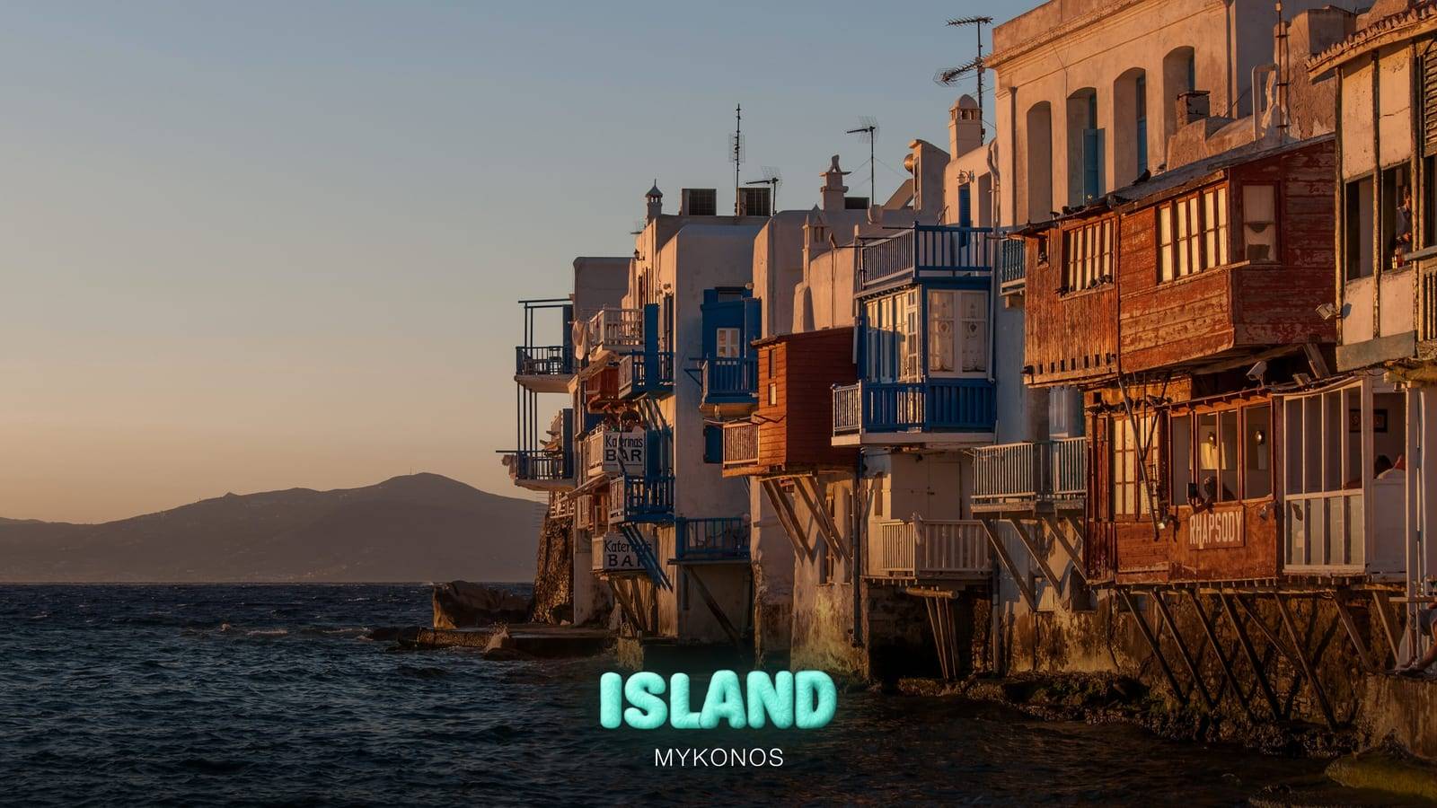 The balconies of Little Venice over the sea in Mykonos Town at sunset, with the Party Island Mykonos logo