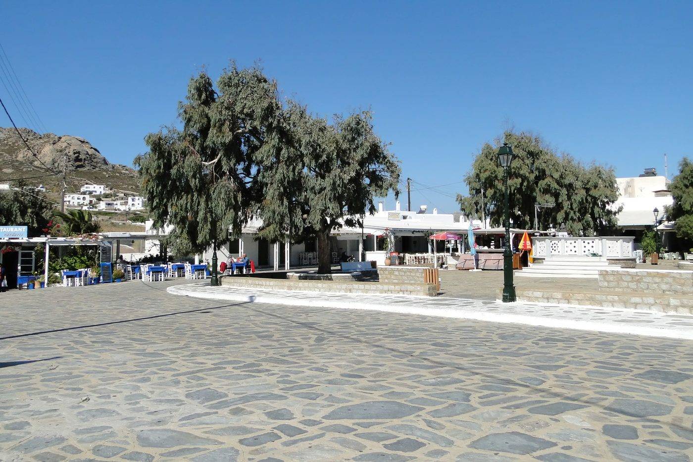 The paved main square of Ano Mera, the inland village of Mykonos, shaded by trees