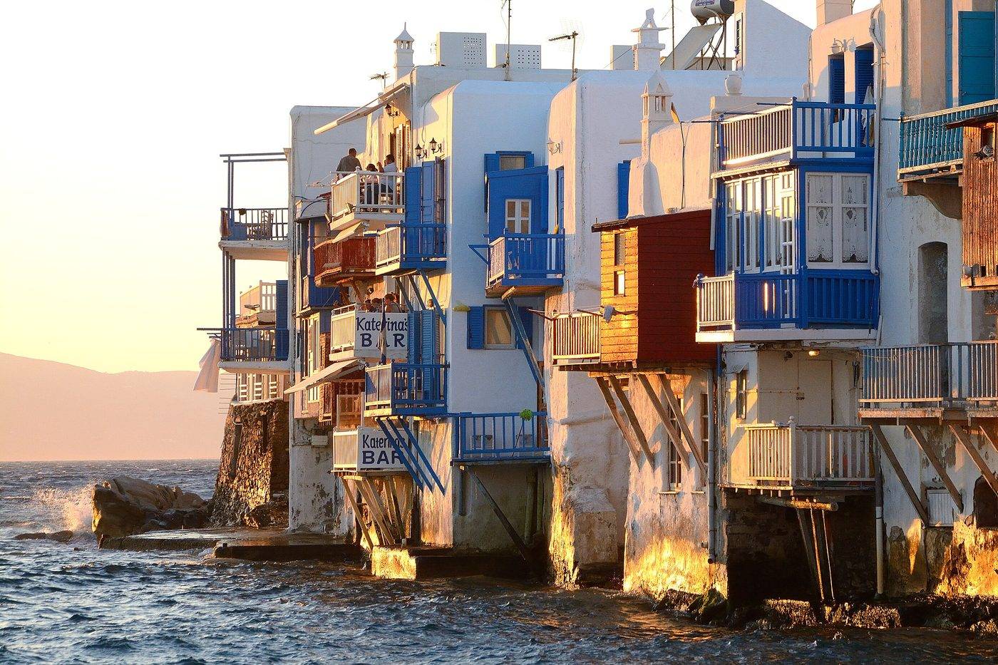 The houses of Little Venice lit gold by the evening sun, with waves below the wooden balconies