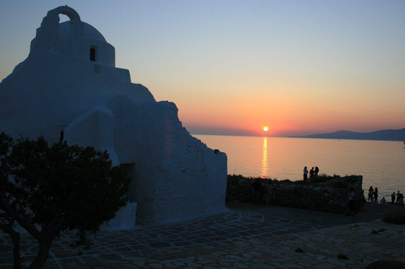 The silhouette of Panagia Paraportiani at sunset, with the sun setting into the sea