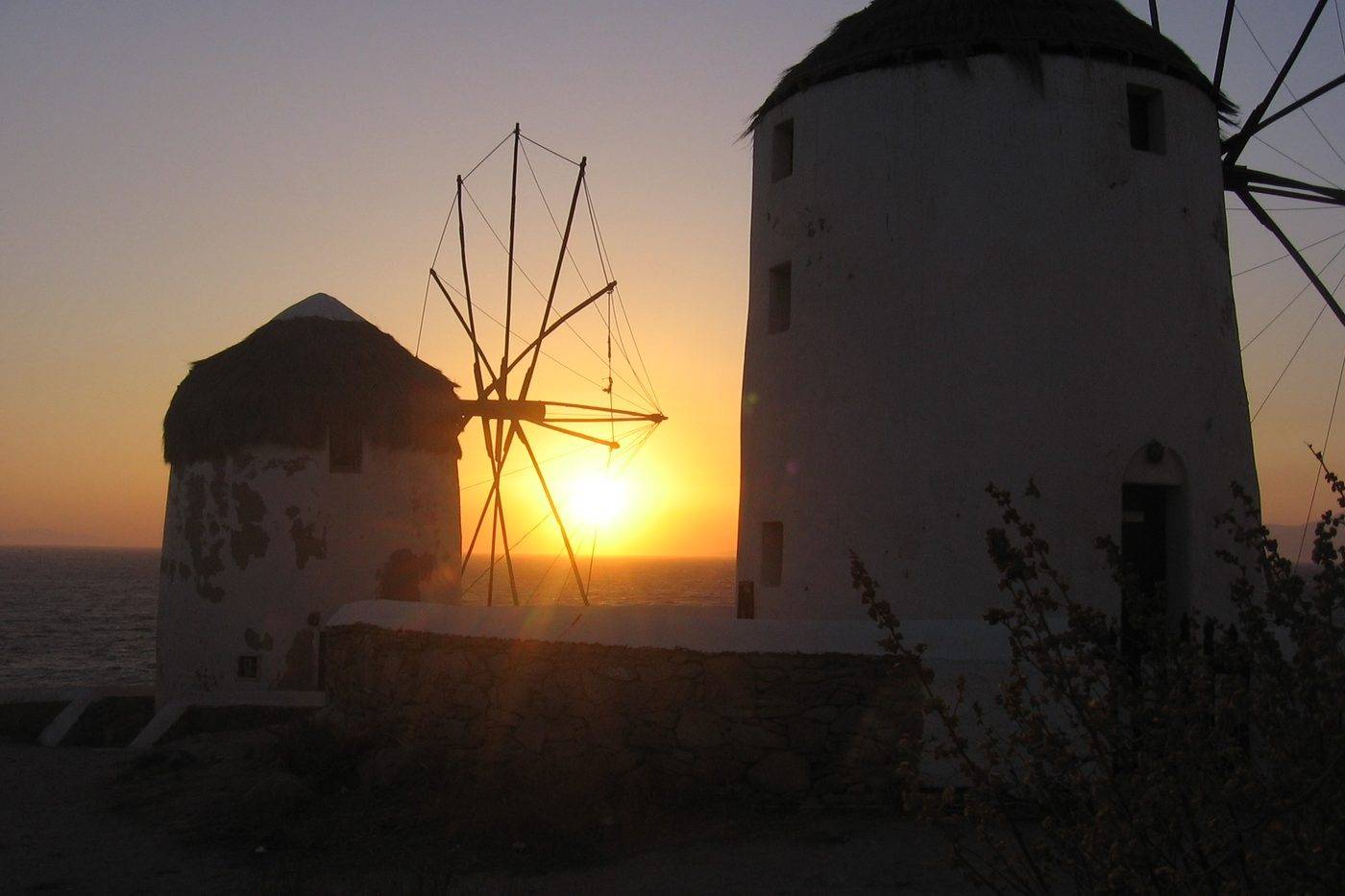 Two Mykonos windmills against the setting sun, the sky glowing orange over the sea