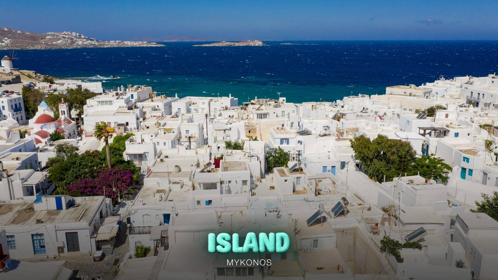 Aerial view of the whitewashed houses and churches of Mykonos Town (Chora) with the Aegean Sea behind, with the Party Island Mykonos logo